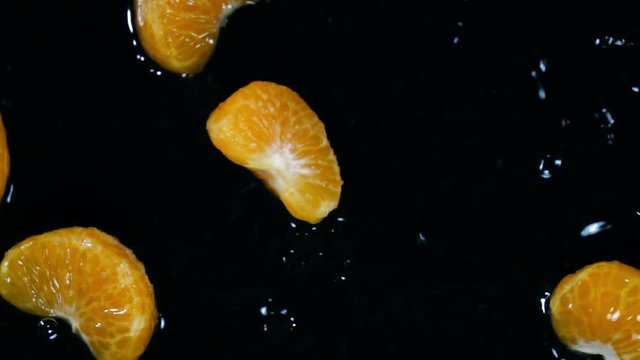 Segments of peeled mandarines falling and splashing in extreme slow motion. Shooting with high speed camera. Overhead top view.

