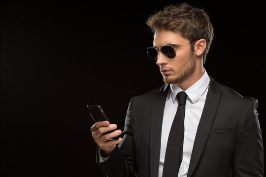 Handsome young man in a suit using his smart phone on black background