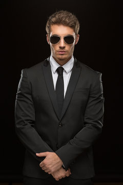 Handsome serious young man in a suit and sunglasses on black background