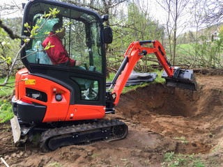 Small excavator with man inside, at work making garden pond