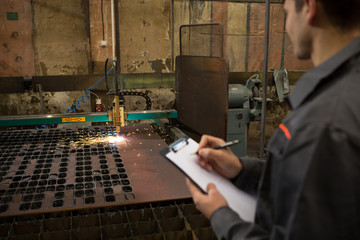 Industrial worker operating plasma cutter at the metal factory