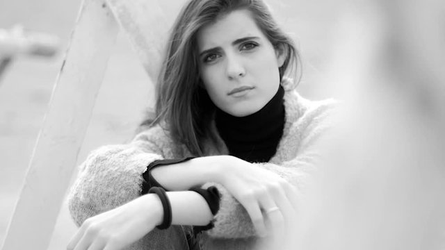 Gorgeous sad lonely woman thinking sitting on sand  black and white looking camera closeup