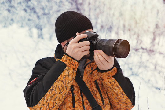 The young man, a photographer takes pictures on the camera in the winter sunny day on a blurred background at the forest,