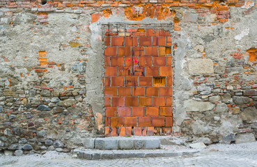 Unplastered stony wall with bricked up door. Blocked entrance to old desolated building 
