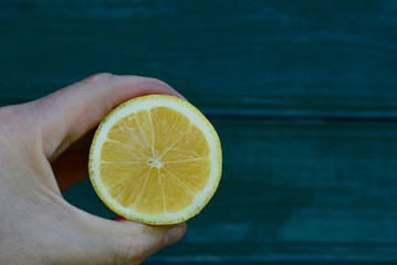кусок лимона в руке на фоне зелёной стены