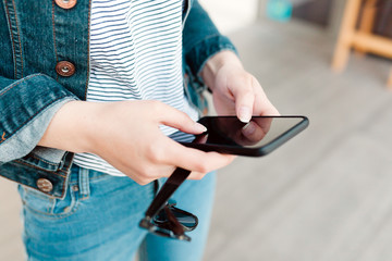 Female hands holding black smartphone and sunglases.