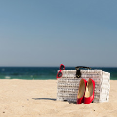 Summer vacation at sea. White wicker suitcase and women's accessories and shoes on the beach.