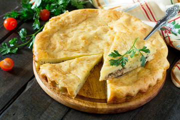 A classic quiche Lorraine pie with potatoes, cabbage, fish and cheese on a wooden table.