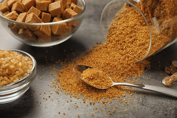 Brown sugar in spoon and dishware on gray background