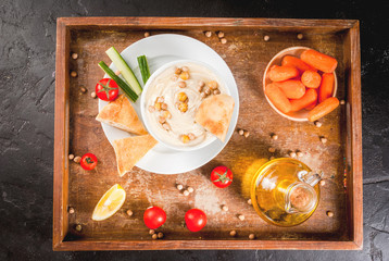 Healthy food. Vegetable sources of protein. Bowl of hummus, on black stone table, with greens, boiled and raw chickpeas. With fresh cucumber, tomatoes, carrots and bread pita. Copy space top view