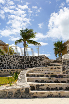Stairs to the luxury resort on the beach. Palm trees and blue sky. White sand beach. Shore of the Caribbean sea. Luxury vacation concept image.