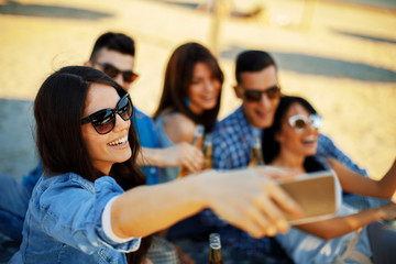 Happy young people having fun on the beach drinking beer and doing selfie