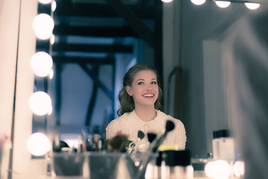 Smiling pretty young woman retro 1940s style looking in theater mirror.
