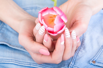 A beautiful female manicure in pink, with a tulip flower against the background of blue jeans