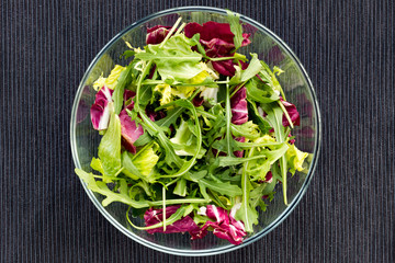 Fresh green salad in glass bowl on black background.