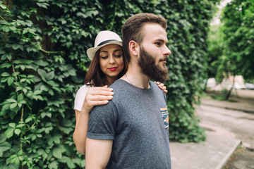 Young and stylish couple walking on the street of summer. Bearded boy and fashionable girl are loving and flirting.