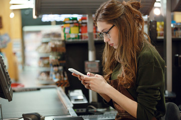 Cashier lady on workspace in supermarket shop using mobile