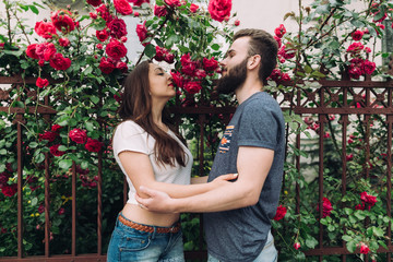 Beautiful and stylish couple of young woman and bearded man near the roses in summer of sunny day.