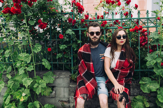 Beautiful and stylish couple of young woman and bearded man near the roses in summer of sunny day.