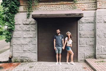 Fototapeta na wymiar Young and stylish couple walking on the street of summer. Bearded boy and fashionable girl are loving and flirting.
