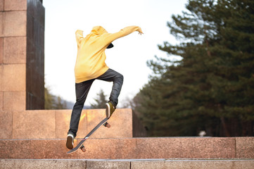 The teenager in a sweatshirt and a cap jumps with a board in the city against the backdrop of the urban sunset light. Photo of extreme