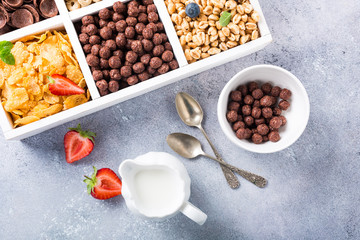 Variety of cold quick breakfast cereals with berries in white wooden box, healthy eating for kids, overhead shot