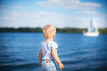 The boy looks at the ship floating on the river