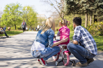 Happy young couple teaching daughter to ride a bicycle on beautiful sunny day