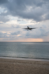 Fototapeta na wymiar View from the sandy beach on the landing airplane isolated above the sea over beautiful cloudy sky background