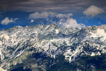 Fototapeta premium Cloud covered Jof di Montasio (Montaz) and Jof Fuart (Vis), the peaks of the Italian part of Julian Alps, rise above the Slovenian ridges in Trenta valley, seen from Kanjavec, Triglav National Park