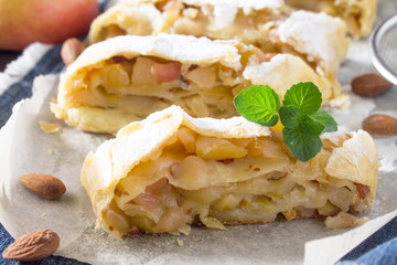 Homemade apple strudel with fresh apples, nuts and powdered sugar on a blue vintage wooden background. Country style apple strudel.
