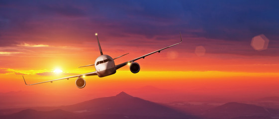Naklejka premium Komercyjny samolot latający nad górami w zachód słońca