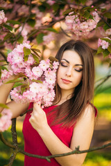 Beautiful girl posing to the photographer against the background of blooming pink trees. Spring. Sakura.