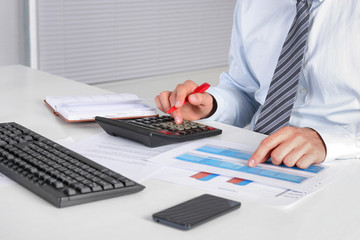 Cheerful young businessman sitting at the table with laptop and stretching in the office