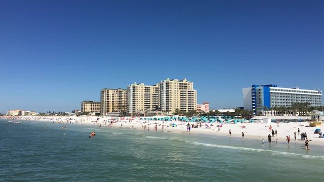 Tourists play on the white sands of Clearwater Beach, Florida with hotels and condominiums in the background.