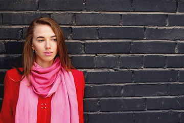 young attractive woman in red coat on dark brick background