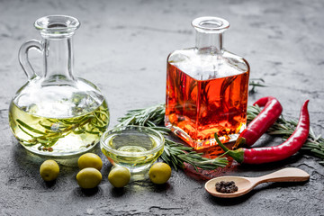 Bottles with chili and olive oils and herbs on stone background