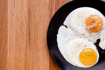 two fried egg on black plate on wooden table