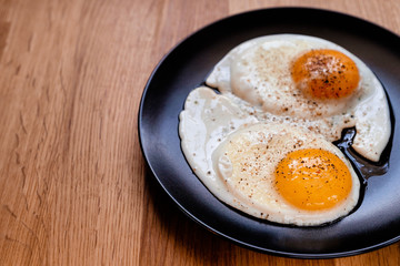 two fried egg on black plate on wooden table