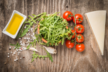 Arugula, tomatoes,cheese and oil on rustic table as background