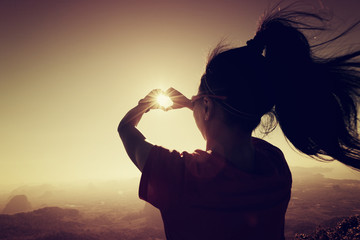 silhouette of successful woman hands making a heart shape on sunrise mountain top
