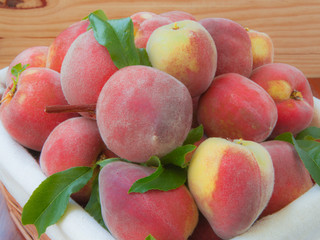 Ripe peaches in basket on wooden background.