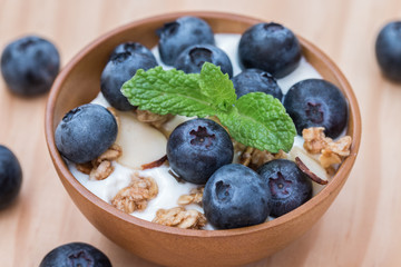 Yogurt with granola and organic blueberries in wooden bowl.