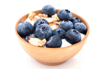 Yogurt with granola and organic blueberries in wooden bowl.