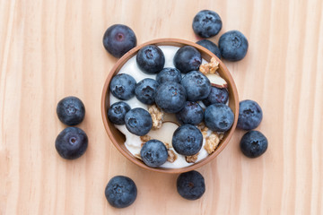 Yogurt with granola and organic blueberries in wooden bowl.