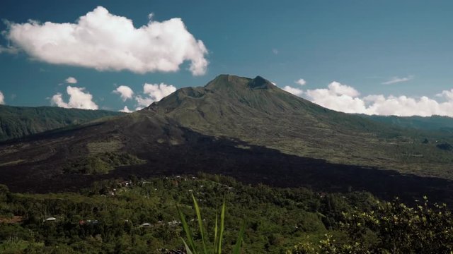 Mount Batur volcano view from Kintamani on sunny summer day with blue sky and small clouds in Bali, Indonesia. Shot with Sony a7s on slider. Slide from stone wall