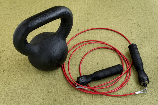 Black Kettle Bell And Red Jump Rope On A Light Green Background

