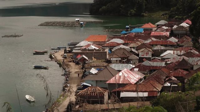 View of traditional Trunyan village on eastern shore of Lake Batur on sunny summer day. Small fishing boats and bamboo fish farms in water. Shot with Sony a7s on tripod in Bali, Indonesia