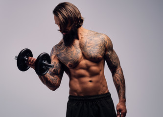 A man with long hair and tattoo on his torso holds dumbbell.