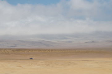 Lonely car driving through the desert under cloudy sky